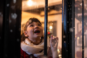 Adorable child look through the window and admiring first snow flakes.
