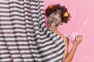 Hygiene procedures and routines concept. Joyful curly haired woman enjoys showering applies beauty...