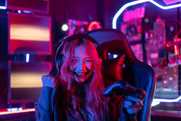 You win. Gamer using joystick controller plays online video game with computer neon lights backgrounds, woman use gaming headphones playing live stream esports games console at home.