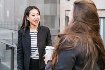 Positive young ethnic female office worker in formal outfit listening to colleague standing with...