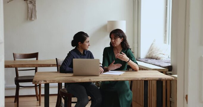 Skilled diverse women workmates brainstorming ideas sit at desk with laptop in office. Meeting of client and sales manager, worker make commercial offer to customer. Team-work, collaborative project