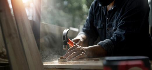 The carpenter uses a hammer hit the nails on the wood at shop. Dark tone color. concept of craftperson and skilled manual labour. © NAMPIX