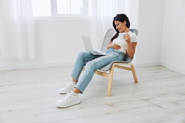 Woman relaxing at home sitting in a chair and watching a movie on her laptop with a cup of tea, happiness and laughter comedy, freelancer lifestyle