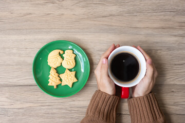 Merry Christmas with woman hand holding coffee cup and homemade cookie on table. Xmas eve, party, holiday and happy New Year concept