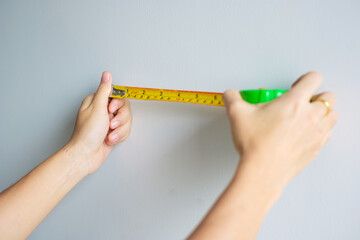 Man hand using tape measure for measuring with wall backgrounds at home. DIY, Interior design, repairing and improvement home or apartment concepts