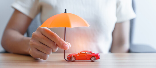 Businesswoman hand holding orange umbrella and cover red car toy on table. Car insurance, warranty, repair, Financial, banking and money concept