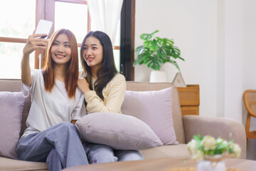 Relax at home concept, LGBT lesbian couple is smiling and using smartphone to selfie together