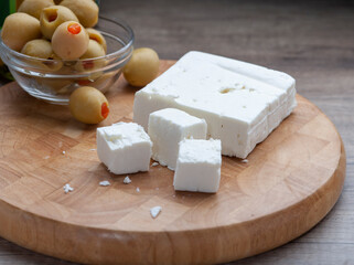 Greek Feta Cheese on wooden cutting board with green olives