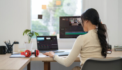 Rear view of young woman editing video footage on professional computer at her workstation.