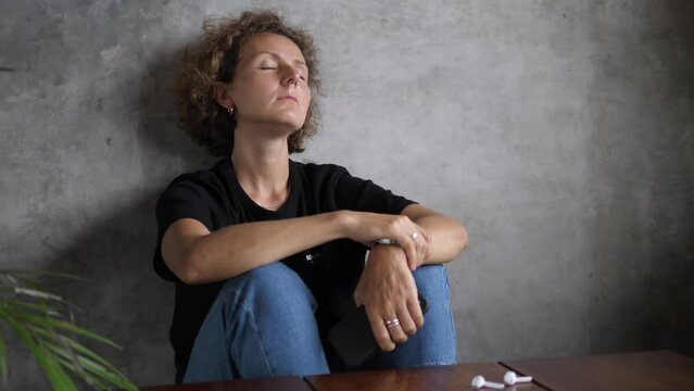 A woman sits on the floor against a gray wall in a state of depression and in a complete breakdown of strength and energy. She is trying to gather the rest of her strength and take action.