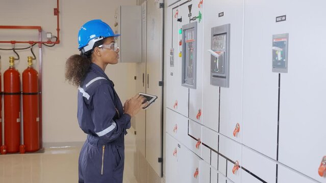Electrical young asian woman engineer examining maintenance cabinet system electric and using tablet in control room at industrial factory, technician or electrician inspection power distribution.