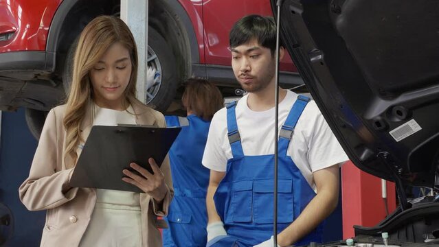 Mechanic giving contract document customer asian woman signing about car with repairing in garage, auto service, technician and client doing agreement about problem of vehicle, transport concept.