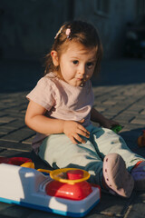 A little baby girl having fun playing with a toy kitchen, sitting at the sunset in the backyard. Toys for children, ideas for kindergarten children. Creative