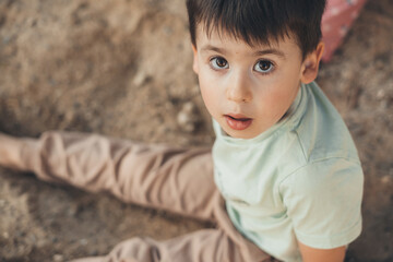 Portrait of a boy sitting in the sand looking into the camera. People lifestyle concept. Happiness concept. Family lifestyle concept. Family activity concept