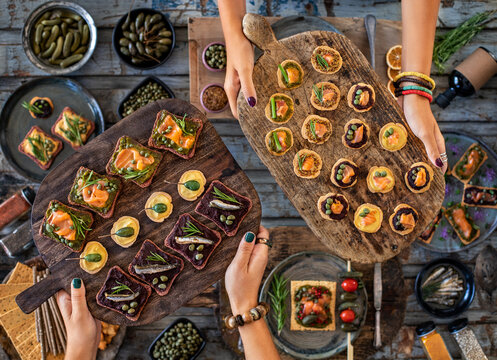 Sea food tapas and ricotta toast with capers at the hands of two women.
