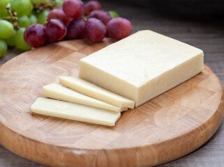 Mild white cheddar on wooden board with grapes