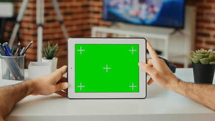Male student looking at horizontal green screen on display, working with digital gadget at home. Using isolated chroma key template and blank copy space with mock up on tablet. Close up.