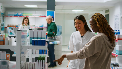 Asian pharmacist talking to diverse customers with disease, giving pharmaceutical products from pharmacy shelves. Employee giving medical assistance to people, explaining medicaments in drugstore.