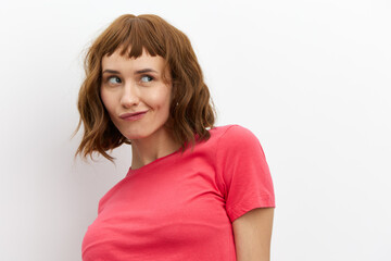 Obraz premium a funny, mischievous woman in a red T-shirt stands on a white background playfully looking away