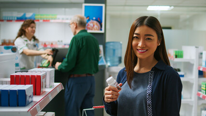 Smiling asian customer checking medicaments packages on shelves, looking at healthcare products to...