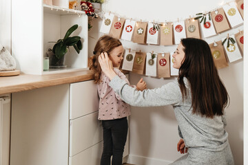 Mother with child opening Christmas advent calendar tasks and gifts. Toddler girl excited about festive surprise in craft bag at home. Family celebration and preparation for New Year