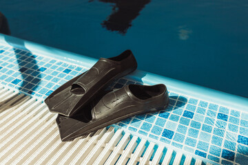 Pair of swimming flippers placed on tiled floor on edge in pool in sunlight   © Dzmitry