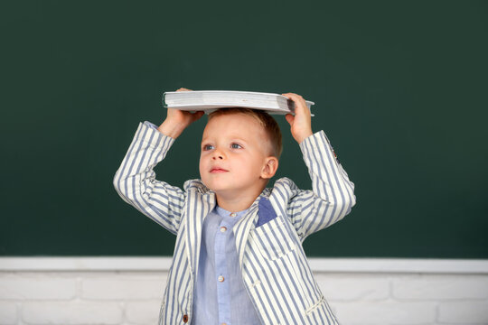 School child student learning in class, study english language at school. Portrait of funny schoolboy in classroom near blackboard. Cute school boy with book.