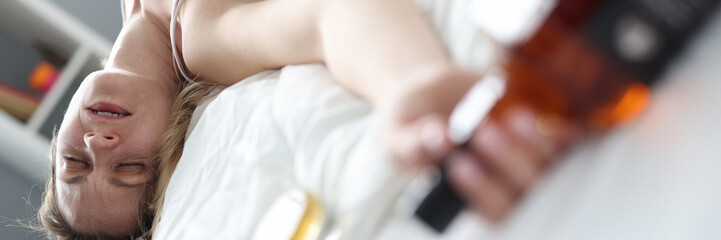 Drunk woman sleeping with bottle of alcohol in bed closeup
