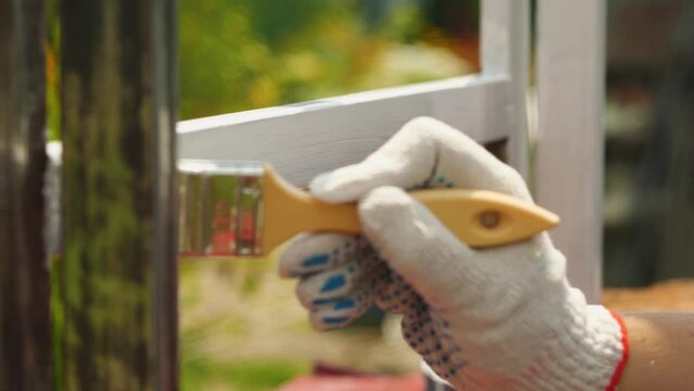 A hand in a rag glove paints a metal profile with a brush with white oil paint. Outdoor work. Protecting metal square pipes from rust and corrosion. Selective Focus
