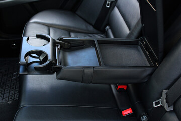 Armrest in the car with cup holder for rear seats row. Leather armrest for storing things, moves and opens in the interior of the car. 