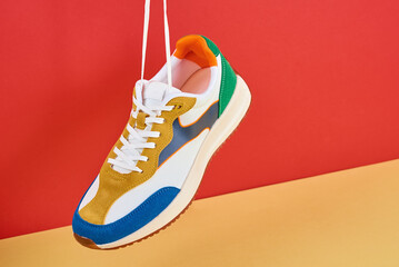 Hanging fashionable sneakers on colorful background. Stylish sports casual shoes. Creative...