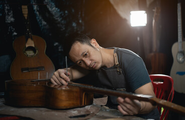 Guitar makers asian man making acoustic guitars in laboratory. Asian guitar maker builds high...