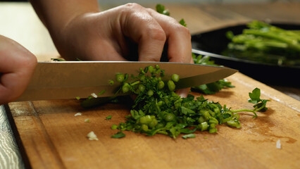 Close-up of a chef's hands with a knife slicing parsley on a cutting board. Side view. Delicious and healthy food.