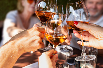 Family celebrating at dinner. Detail of hands while toasting with glasses of orange wine in a sunny...