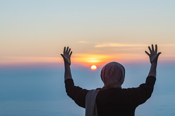 Human with hands open palm up praying to God on the mountain sunset background.