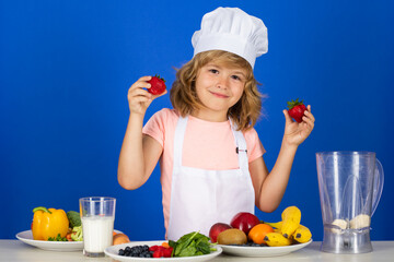 Kid boy in chef hat and apron hold strawberries cooking preparing meal. Little cook with vegetables at kitchen. Natural kids food.