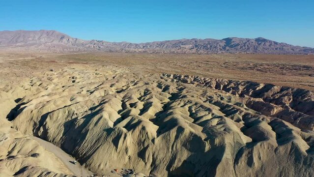 Aerial Landscape Drone Flying Over Hilly Arroyo Tapiado Mud Caves Towards Mountains on Hot, Dry, Sunny Day with Blue Skies