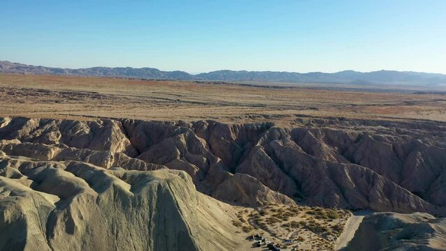 Aerial Landscape Drone Slider Shot Flying Over Hills Arroyo Tapiado Mud Caves Towards Mountains on Hot, Dry, Sunny Day with Blue Skies