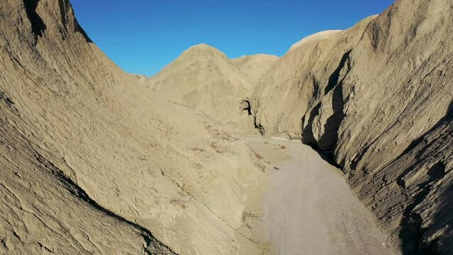 Aerial Flying between hillsides formed by Mud Caves Over Dirt Road on Hot Dry Day - Arroyo Tapiado Mud Caves in Anza Borrego State Park