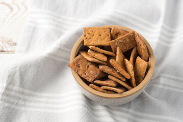 Bowl of dry crackers with tomato and basil on light wood background with napkin