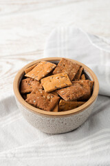 Bowl of dry crackers with tomato and basil on light wood background with napkin