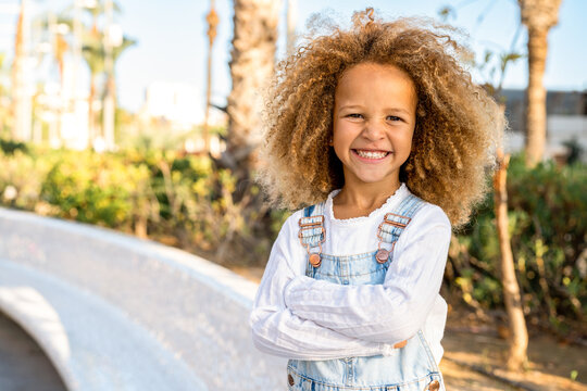 Portrait of beautiful smiling little girl with curly hair close up, against background of summer city park.