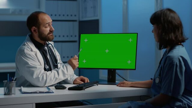 Medic and nurse discussing patient disease report planning medication treatment. Doctor pointing at green screen chroma key mock up computer template while working after hours in hospital office