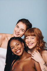 Happy women with different skin tones smiling at the camera in a studio - obrazy, fototapety, plakaty