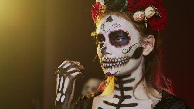 Scary young adult thinking about santa muerte in studio, acting thoughtful and pensive on day of the dead mexican holiday. Woman portraying holy cavalera catrina halloween goddess. Handheld shot.