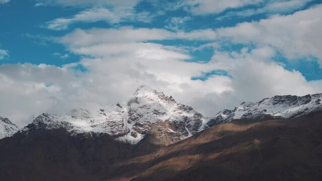 4K shot of clouds moving above the snow covered mountain peaks as seen from Keylong in Lahaul Spiti district in Himachal Pradesh, India. Clouds above the snowy Himalayan mountain peaks in Himachal. 