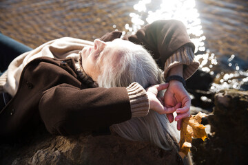 elderly woman with gray hair wearing a brown coat  holds a yellow maple leaf in his hand on the...