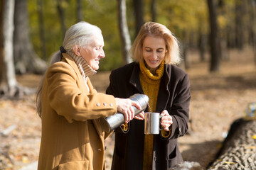 Two woman friends  drinks tea and enjoying a holiday  in autumn outdoor.  portrait of a smiling...