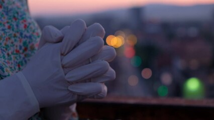 Woman's hands with crossed fingers praying in the city in the evening 
