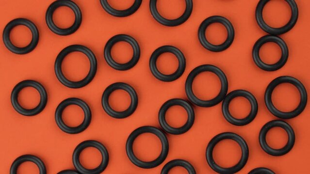 Abstract top view of black round rubber seal gaskets on a colorful orange background. Geometric shapes details close-up. Rotation